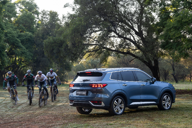 A handsome blue Ford Territory parked in a tree-encircled park with cyclists riding past.
