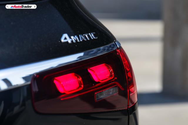 Close-up view of the rear left side of a black Mercedes-Benz GLS450d AMG Line, focusing on the illuminated red taillights and the '4MATIC' badge. The image is taken in daylight with a blurred background that emphasizes the car's details.