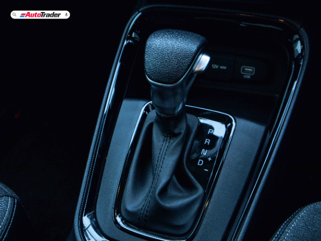 Close-up view of the gear shift lever in a Kia Sonet, showing the automatic transmission with gear positions labeled P, R, N, D, and manual shift options (+/-). The image also includes a 12V power outlet and a USB port in the background.