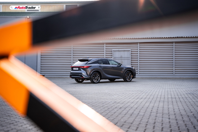 A rear three quarter view of a dark grey Lexus Rx 350 F Sport viewed through railings