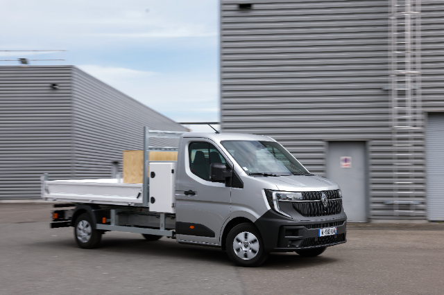 The image shows a silver Renault Master Blue dCi tipper truck parked in an industrial area with grey buildings in the background.
