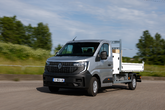 A silver Renault Master Blue dCi tipper truck is driving on a road with greenery in the background.