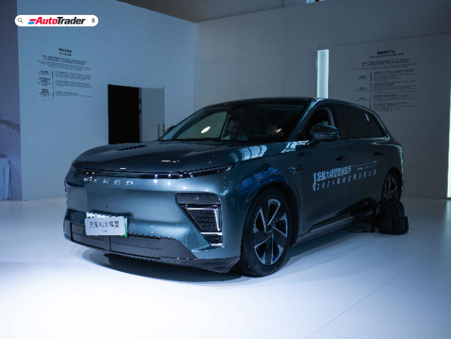 A sleek, dark-colored Exeed electric vehicle (EV) is displayed in a well-lit showroom. The car features a modern design with smooth lines and a futuristic front grille. The word "EXEED" is prominently displayed on the front of the vehicle. The showroom has informational posters on the walls, and the floor is white, enhancing the car's appearance. The AutoTrader logo is visible in the top left corner of the image.