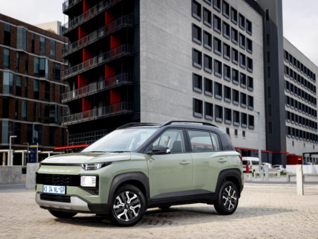 A green compact SUV is parked in front of a modern multi-story building
