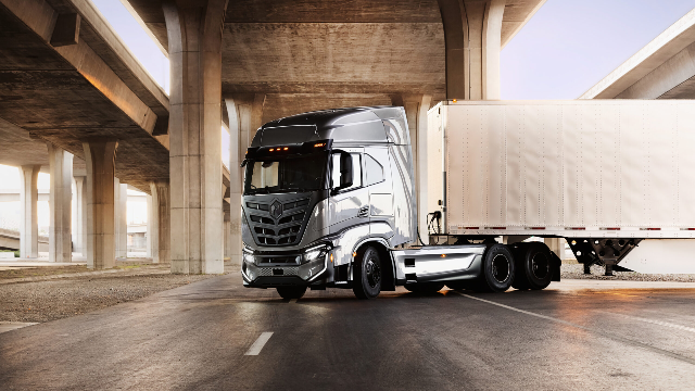 A sleek, modern semi-truck is parked under a series of concrete overpasses.