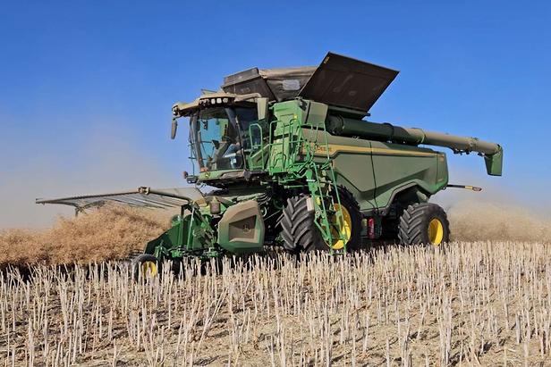A John Deere X-Series combine harvester is operating in a field, cutting and processing crops.