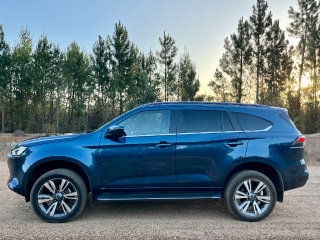 Profile view of the blue mu-X with trees in the background.