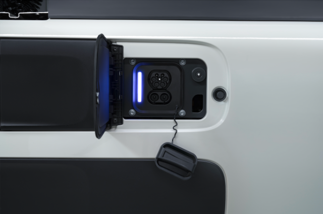 The image shows an electric vehicle charging port with a cover open, revealing the connector and illuminated indicator.