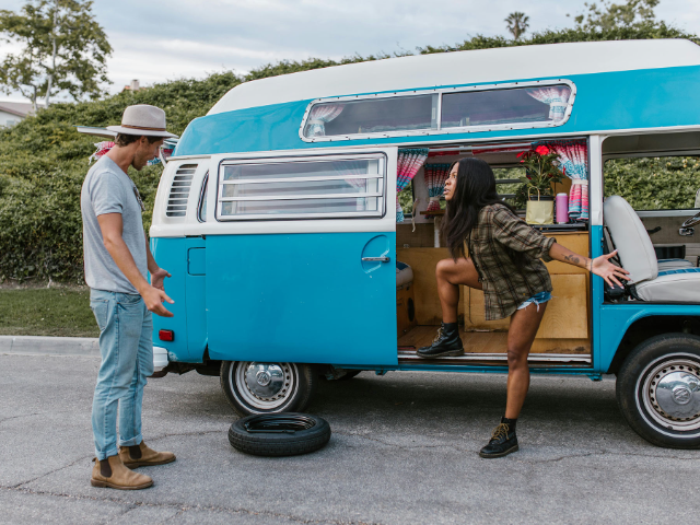 A couple discuss the situation as they look at the flat tyre on their VW bus