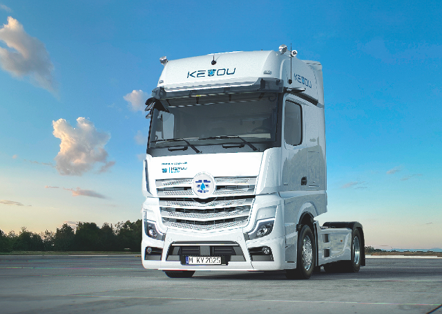 name "KEYOU" displayed on the cab, parked on an open area with a clear blue sky and a few clouds in the background. The truck features a sleek design, and is positioned slightly from the front, showcasing its grille and headlights.