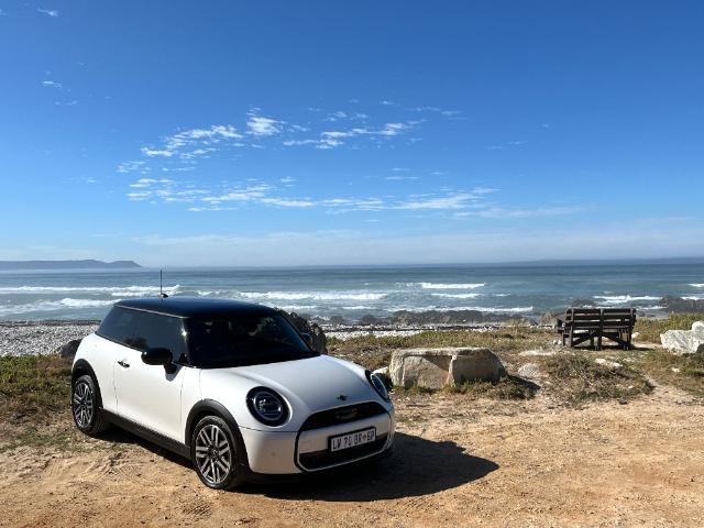 A white MINI with a black roof in front of the ocean.
