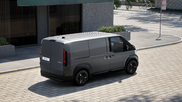 paved street next to a modern building with large windows. The van has a minimalist design, distinguished by clean lines and a tinted rear window.