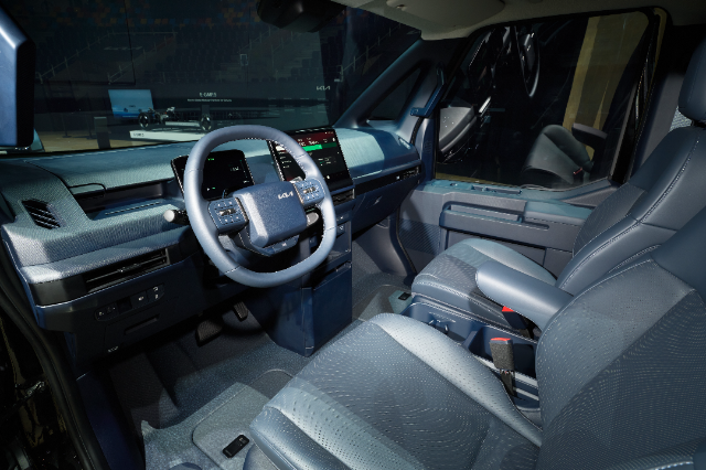 Interior of a modern vehicle showcasing the driver's side. The steering wheel features control buttons, and behind it are digital display screens. The dashboard has a sleek design with a dark color scheme.