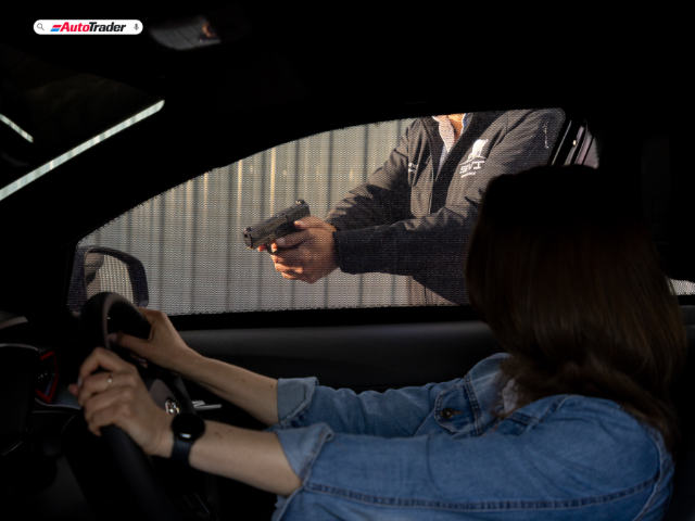 An attacker stands at a car window with a 9mm handgun at the ready