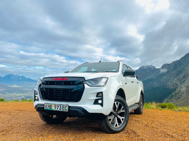 A white Isuzu X-Rider on a dirt road with mountains in the back.