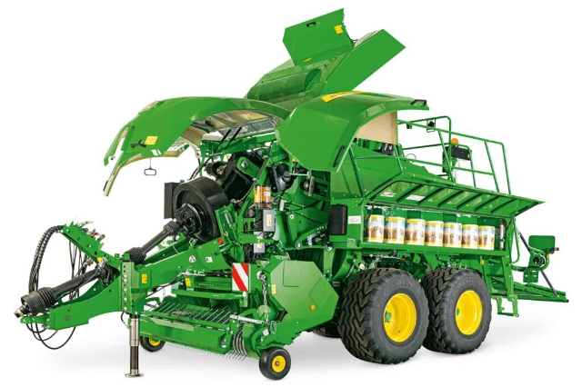 A green John Deere L600 Series large square baler with its side panels open, revealing the internal components and mechanisms. The baler has large yellow wheels, a robust structure, and visible details such as the pickup reel, bale chamber, and various machinery parts. The design is clean and modern, intended for agricultural use.