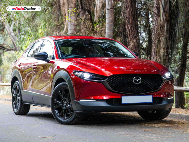 A red Mazda CX-30 parked under shady trees.