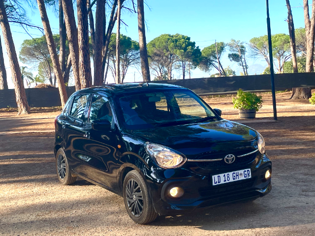 Black Toyota Vitz parked under tall trees.