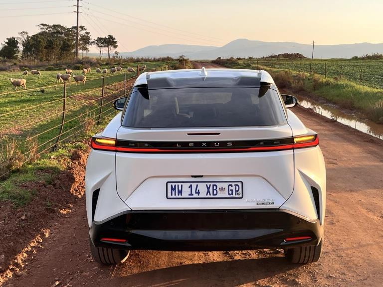 The rear end of the Lexus RZ, taken on a farm road with sheep next to it.