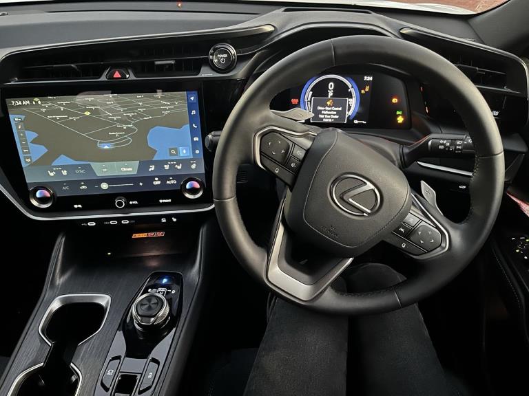 A closer look at the Lexus RZ steering wheel, infotainment screen, digital cluster and rotary dial for switching gears.