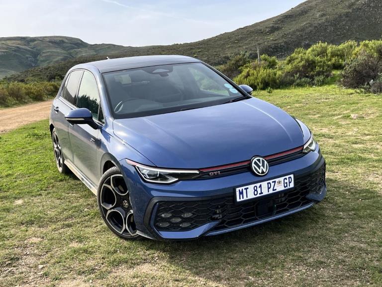 Anemone Blue Golf 8.5 GTI parked on the grass with hills in the background.