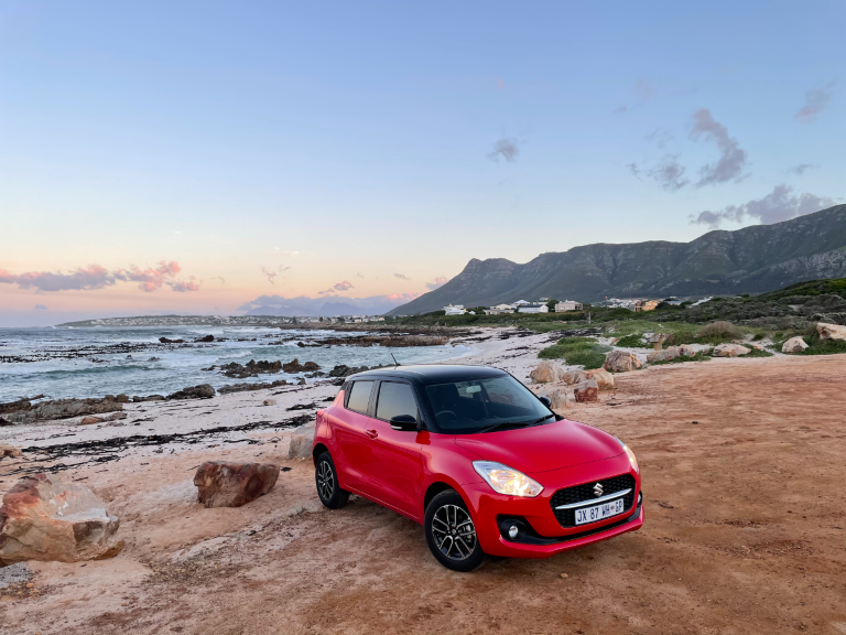 A red, previous-gen Suzuki Swift on the beach.